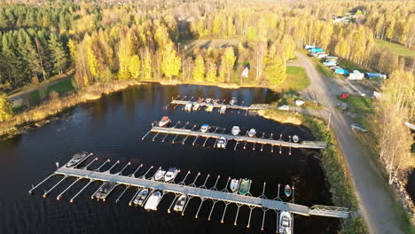 Sweden---A-Quiet-Lake-Bay-with-Boats-on-Still-Water,-Surrounded-by-Beautiful-Autumn-Foliage-Lit-by-the-Setting-Sun---Aerial-Panning