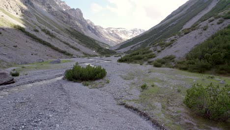 aerial drone footage reversing upwards near a fast flowing river to reveal a dramatic glacial valley surrounded by a steep mountain landscape, pine trees and patches of snow in switzerland