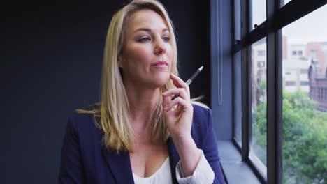 caucasian businesswoman standing looking through a window in modern office