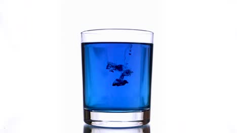 falling of blue inks into glass of blue colored water at bright white background