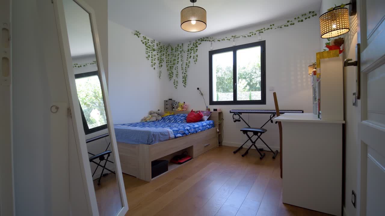 Entrance into a teenager's bedroom, a white desk, a double bed with drawer, a piano and climbing plants as decoration