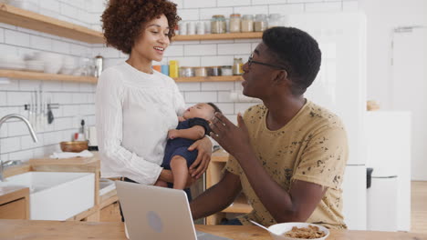 Vielbeschäftigte-Familie-In-Der-Küche-Beim-Frühstück-Mit-Vater,-Der-Am-Laptop-Arbeitet,-Und-Mutter,-Die-Sich-Um-Ihren-Kleinen-Sohn-Kümmert