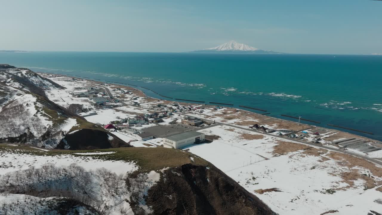 Mount Rishiri Across The Sea As Seen From Snowy Shore Of Wakkanai In Hokkaido, Japan. aerial pullback shot