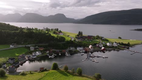 road snakes along coastal edge of fjord with homes on grassy hills with piers and boats docked