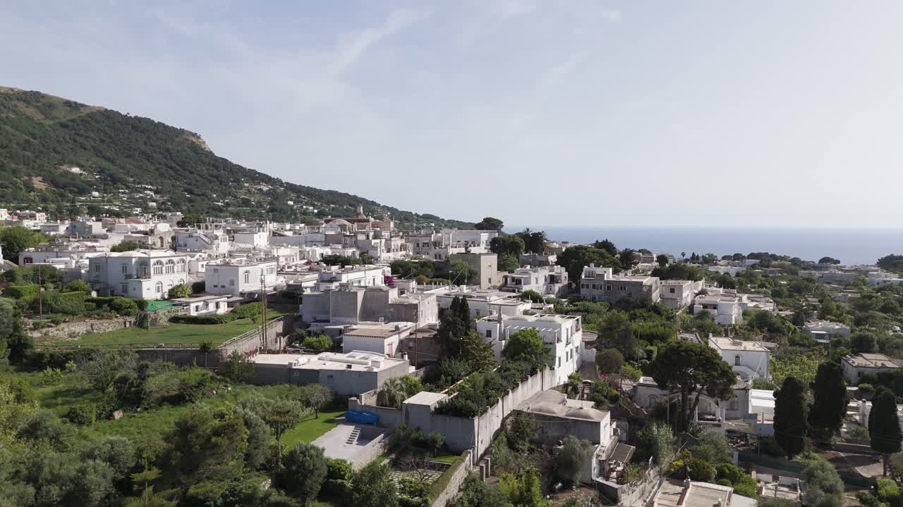 Aerial drone shot rising above Anacapri, unveiling the sea and mountains in the background on Capri Island