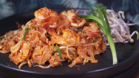 authentic padthai freshly cooked on a black spinning plate close up with prawns and shrimp