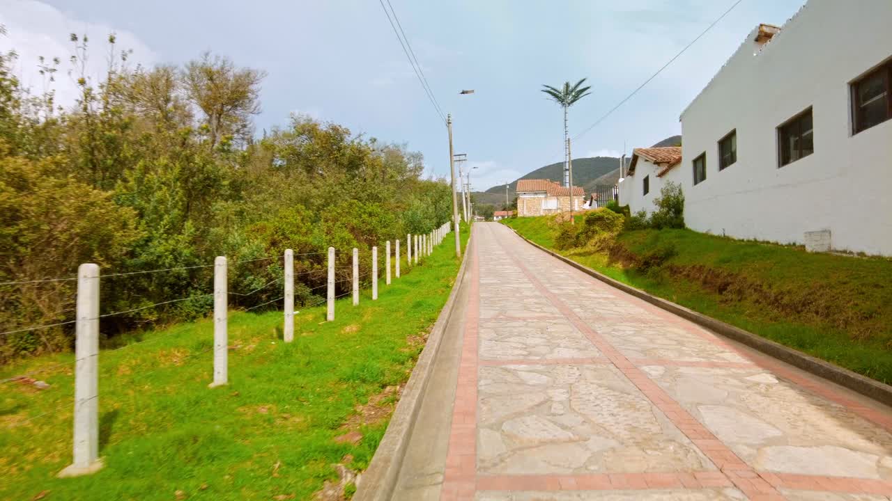 Stone road in Guatavita Colombia with trees, white fences and houses on sunny day