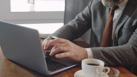 senior businessman typing on laptop at cafe table