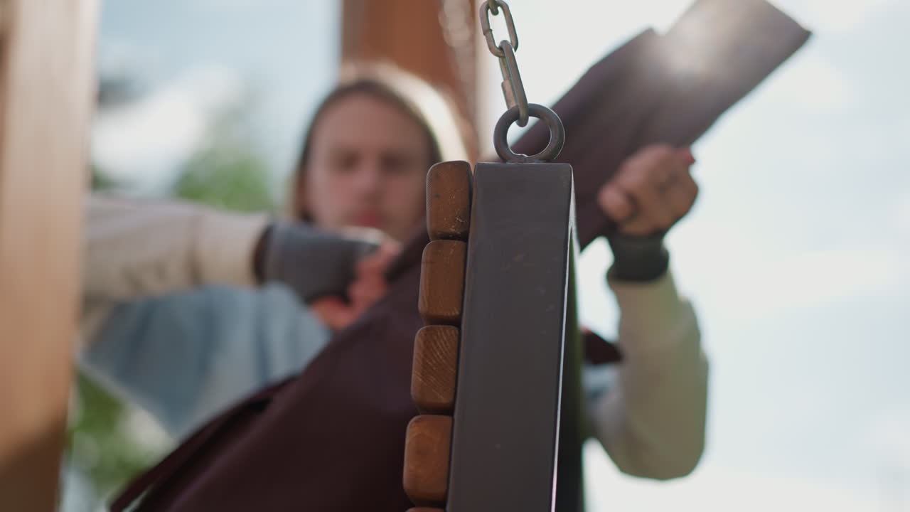 white female guitarist on wooden swing securing guitar case and adjusting strap under sunlight, blurred trees in garden background, rustic chain and wood details, intimate rehearsal mood, casual denim