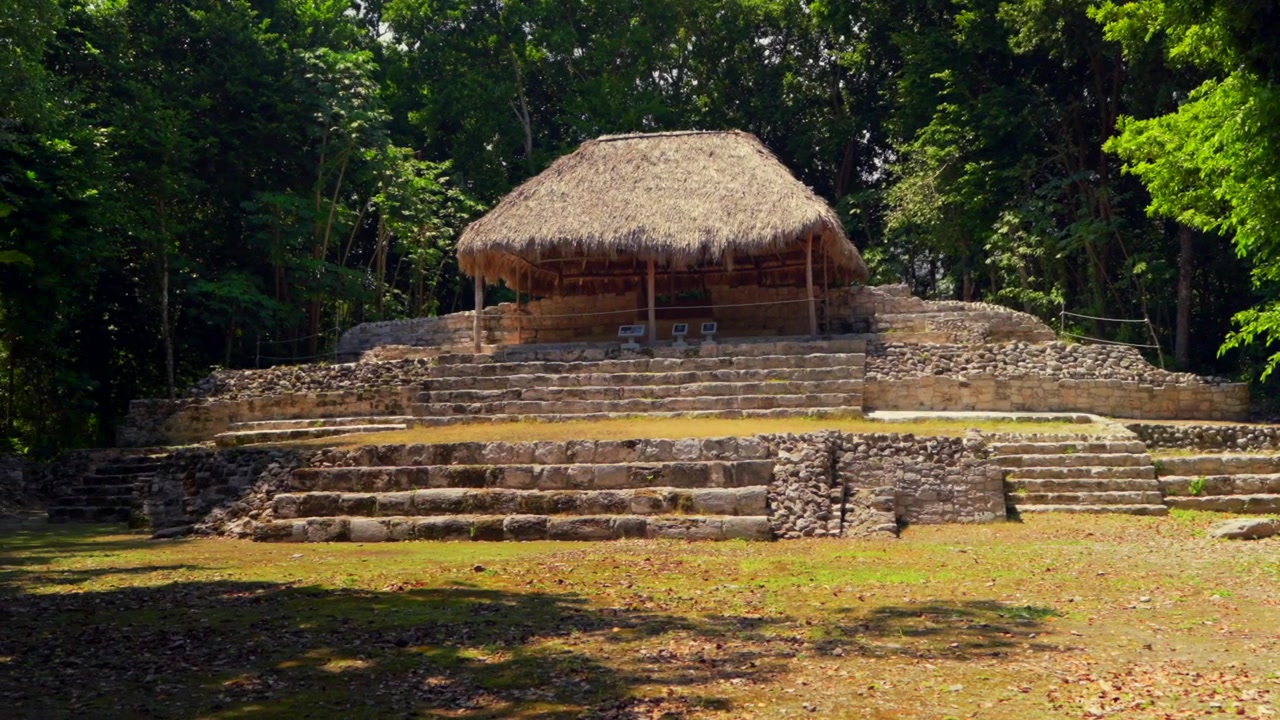 Panoramica che rivela l'antica Struttura Maya IV con un tetto di paglia nel sito archeologico di Oxtankah, circondata da una lussureggiante vegetazione della giungla che rappresenta un ricco patrimonio culturale
