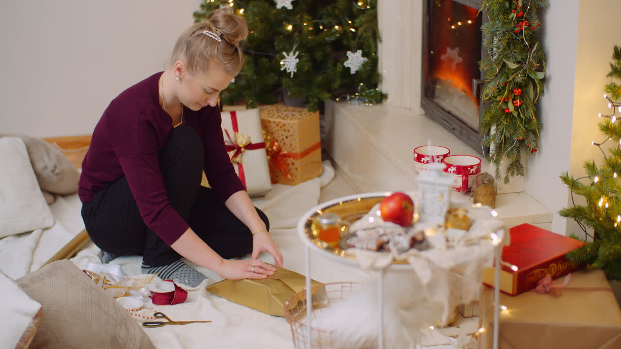 mujer envolviendo regalo de navidad junto a la chimenea en casa 6