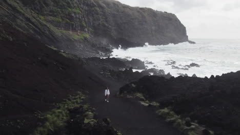 Chica-Caminando-Sobre-Las-Arenas-Negras-De-Ponta-Da-Ferrari,-Azores---Aéreo