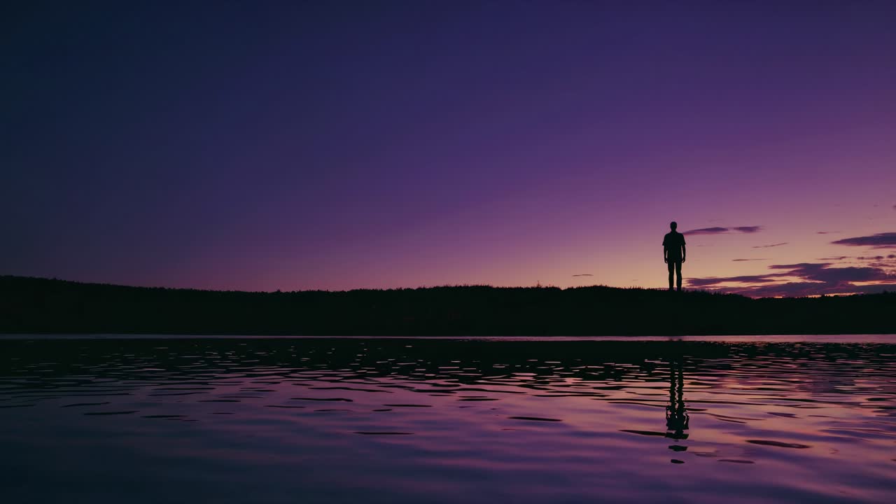 Ihmisen siluetti järven rannalla auringonlaskun aikaan