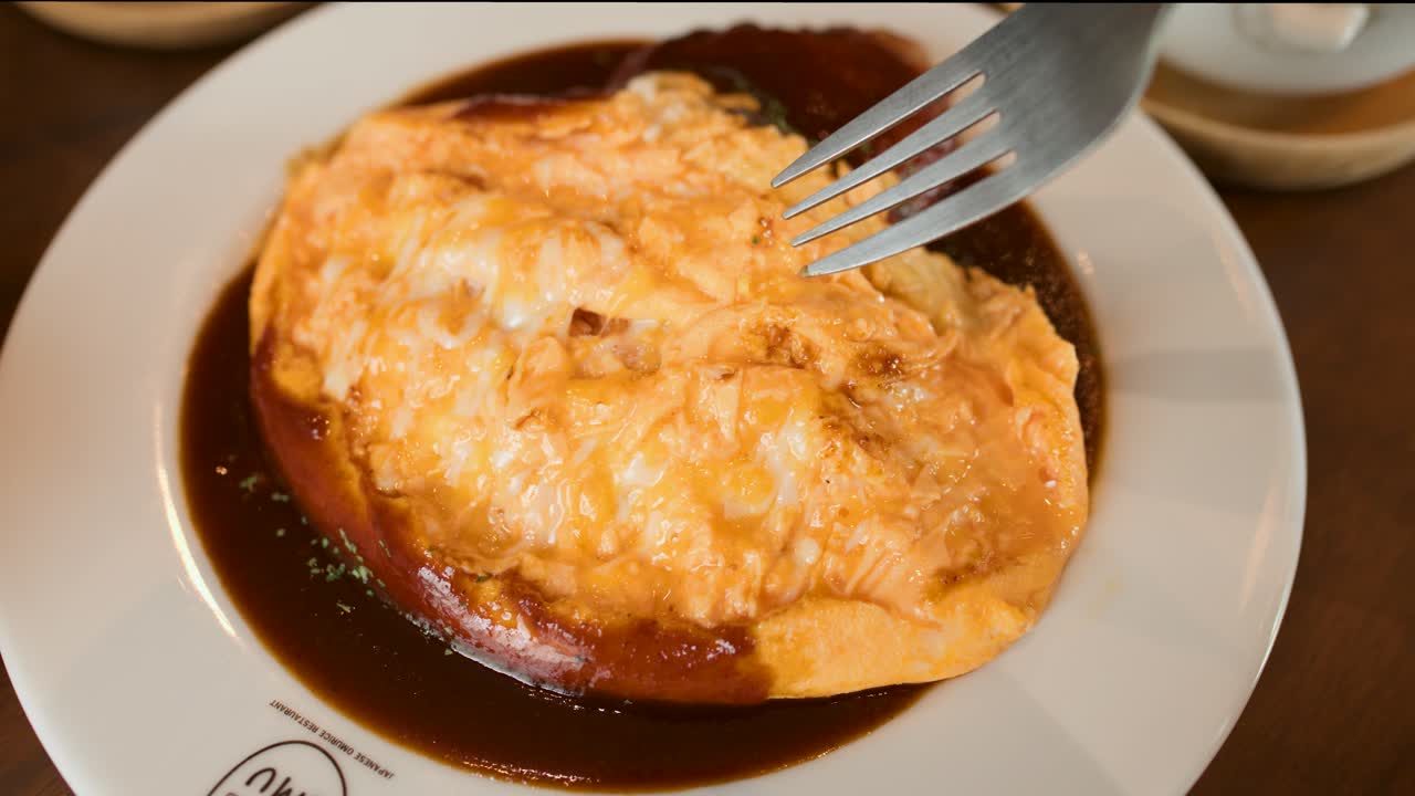 Fork slices into fluffy omelette rice, revealing creamy texture and rich sauce in restaurant lighting