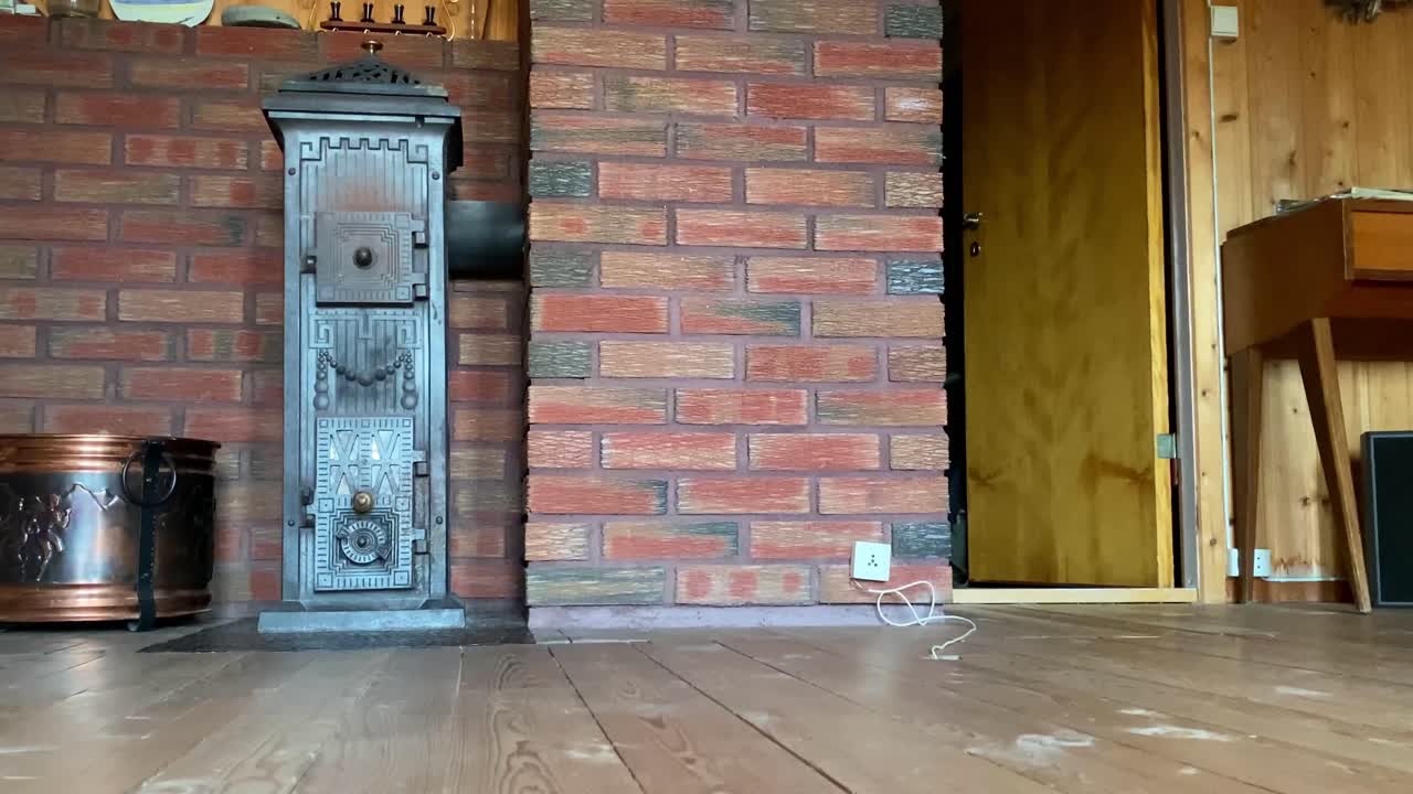 Wood-burning stove set against a red brick wall in a rustic interior with wooden floor and furniture