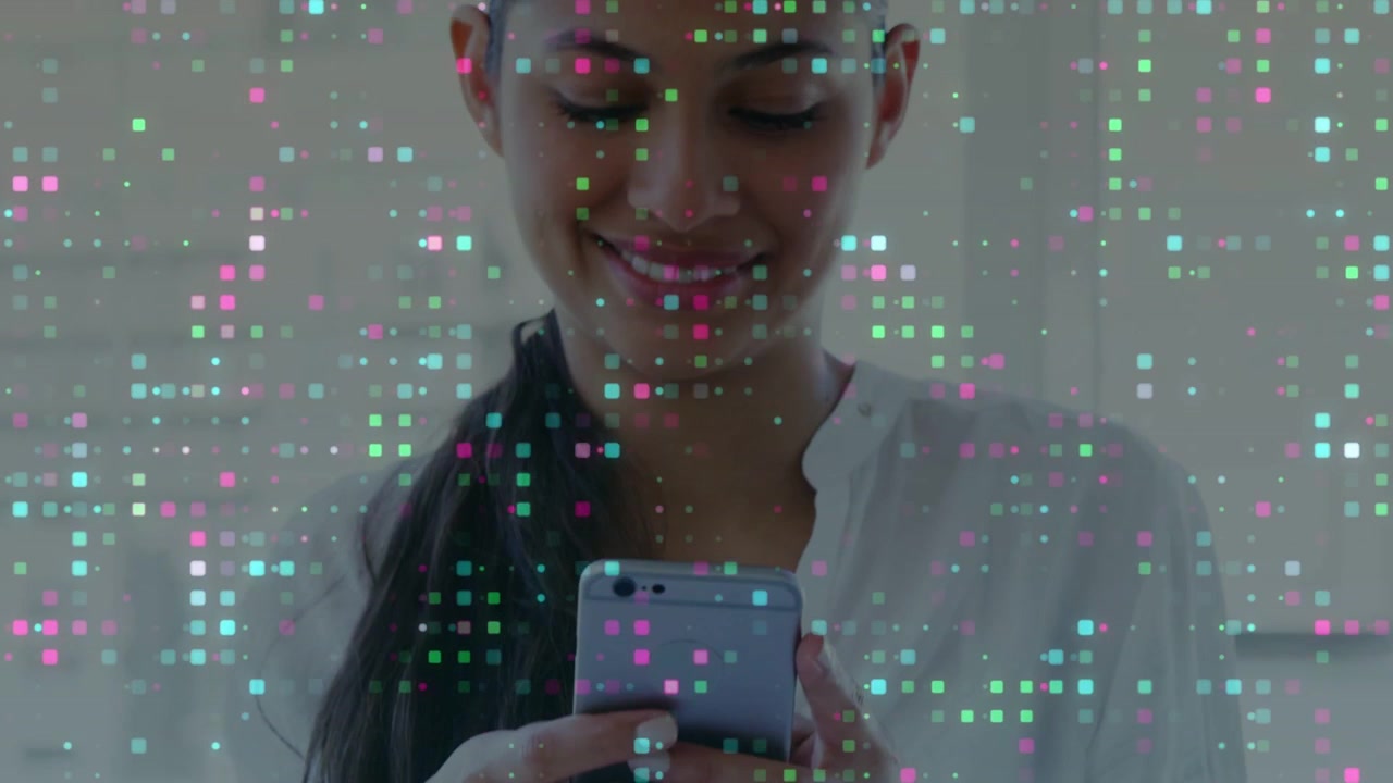 Mujer asiática sosteniendo un teléfono y desplazándose frente al espejo del baño, vistiendo una camiseta clara, con una superposición de píxeles y sonriendo.