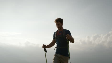 hiker with hiking poles approaches stops and takes his backpack of and starts to open it