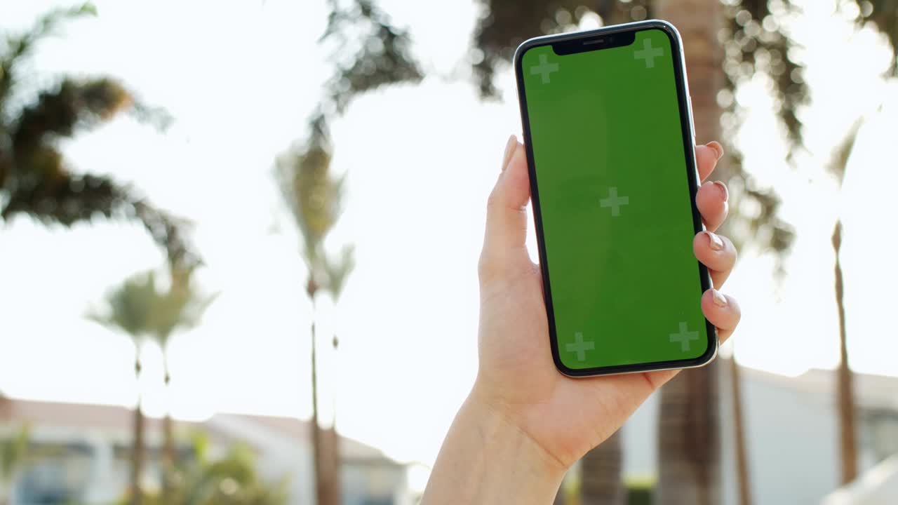 cerca del teléfono inteligente vertical negro con pantalla verde y seguimiento de movimiento en las manos de la mujer caucásica. afuera con palmas en el fondo. llave de croma.