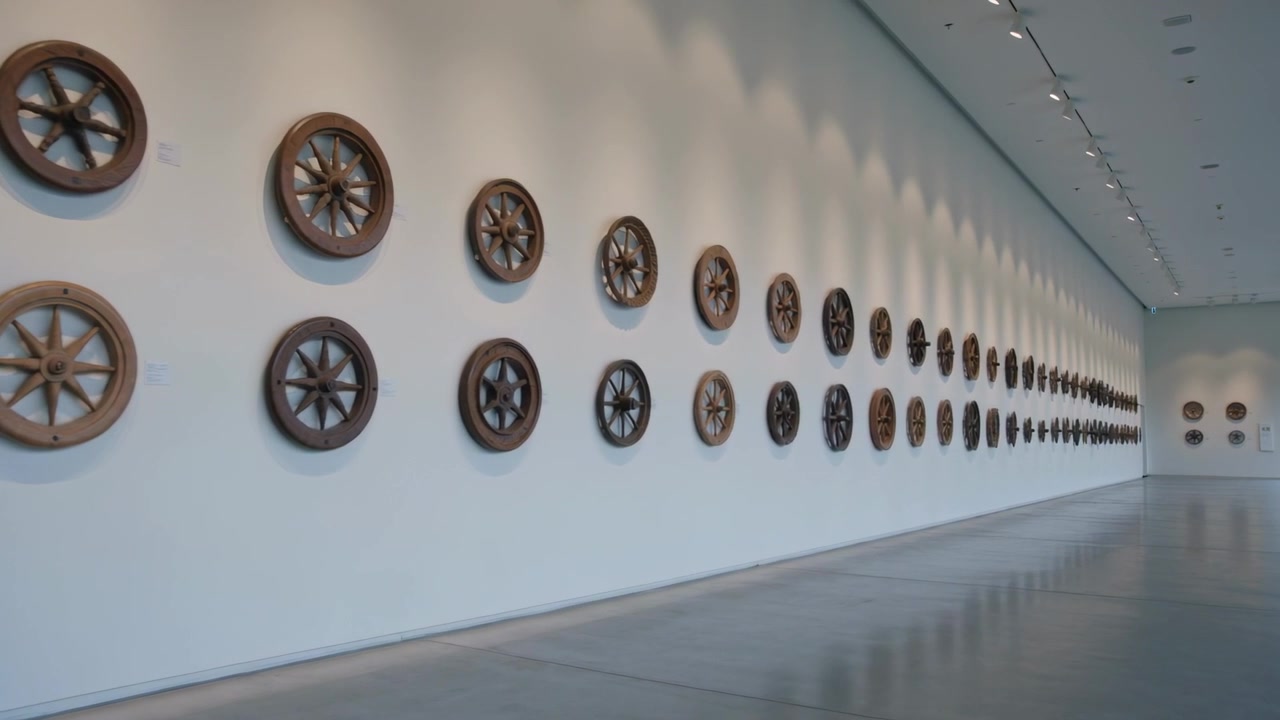 Kameraet begynner å spore til venstre langs galleriveggen, og viser trehjul, eiker og trestruktur i detalj.
