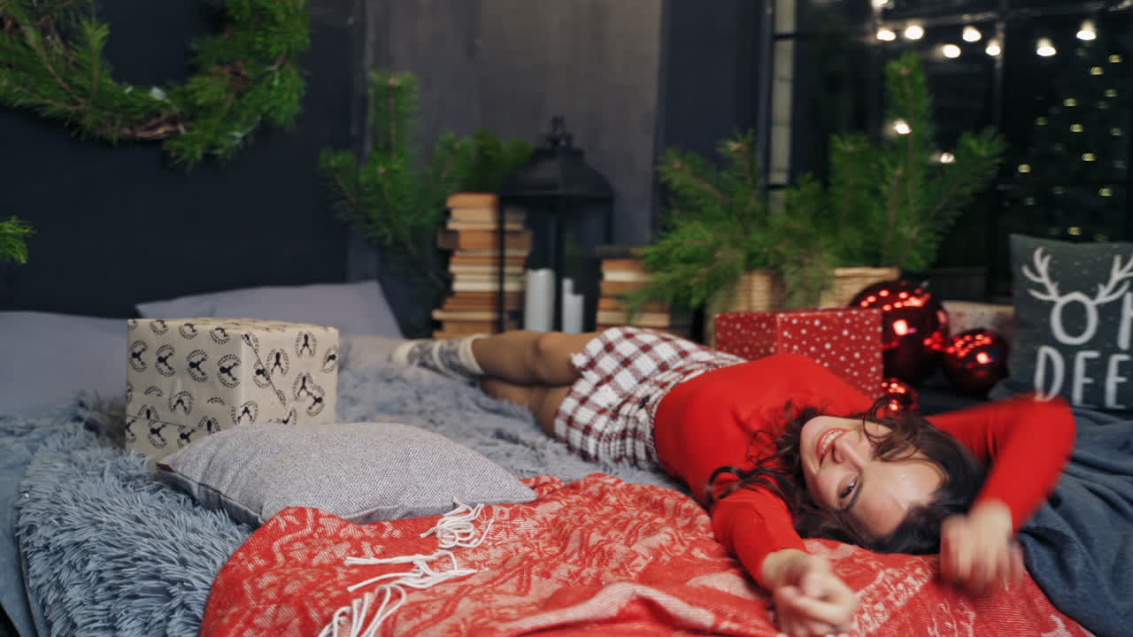 Happy girl enjoys Christmas at home. Young woman on bed resting during New Year. Joyful mood of a pretty female at Christmas.