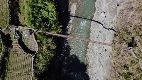 arriba hacia abajo siguiendo el puente colgante de metal que se extiende sobre el arroyo del río de montaña que conduce a senderos granjas empanadas de arroz huertas senderos en un día soleado