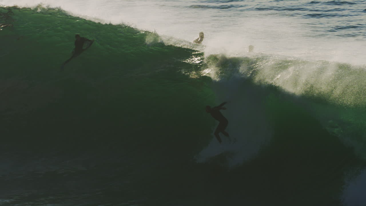 Slow motion view of surfer paddling from base as wave grows and golden hour light sparkles across ocean spray