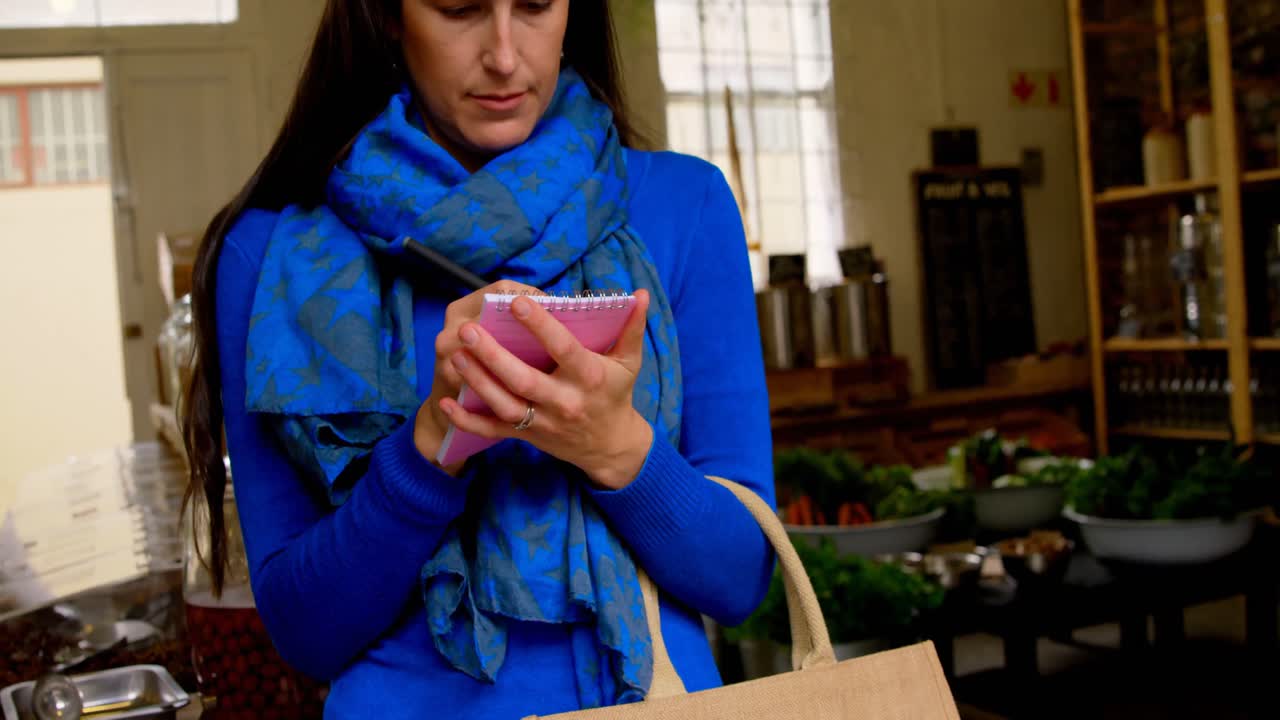 Giovane donna che scrive su un blocco note al supermercato 4k