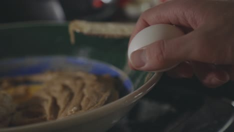 hand breaking egg in a bowl with cookie dough mixture - close up