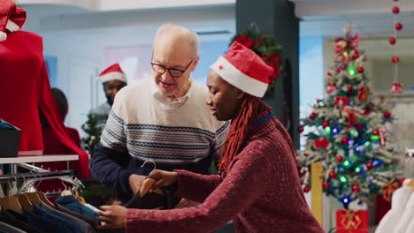 Retail-assistant-helping-older-customer-with-perfect-blazer-pick-in-Christmas-decorated-clothing-store-during-winter-holiday-season.-Employee-offering-fashion-advice-to-client-in-festive-shop