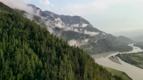 Aerial-ascent-over-forest-to-Squamish-River-and-clouds,-Squamish,-BC,-Canada