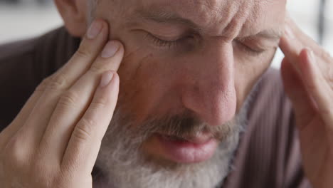 cerca de un hombre de mediana edad que sufre con dolor de cabeza y toca sus sienes mientras se sienta en el sofá en casa