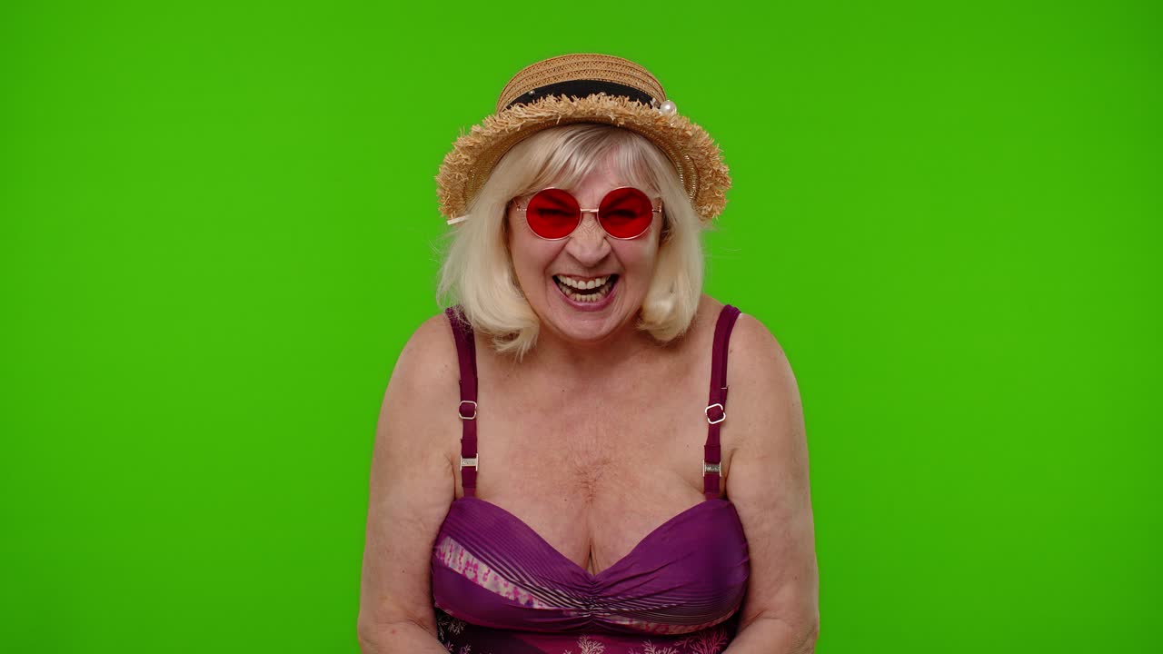 Anziana turista in top del costume da bagno che guarda la telecamera, sorride e inizia a ridere su chroma key.