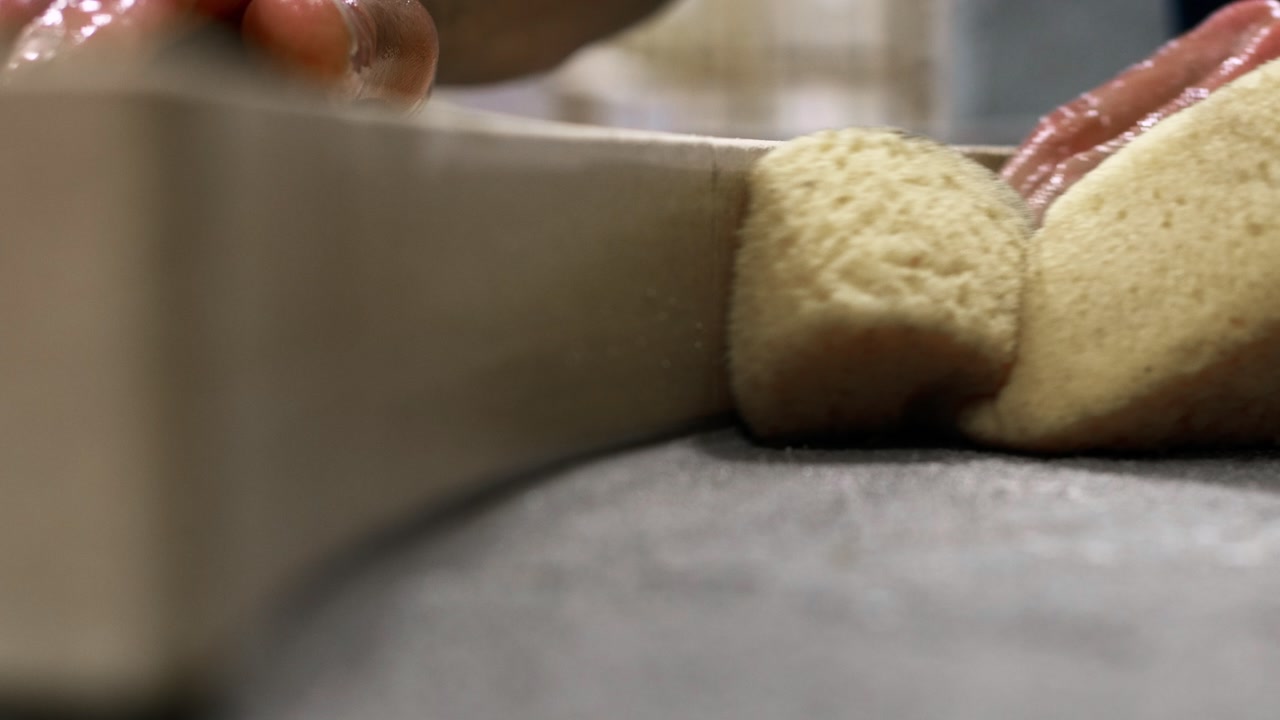 Static extreme close-up shot of a hand using a damp sponge to clean excess grout along the inner edge of a pizza oven during finishing work.