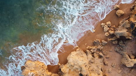 Toma-Aérea-De-Arriba-Hacia-Abajo-De-Olas-Espumosas-Que-Llegan-A-La-Playa-Dorada-Y-Rocosa-De-Portugal