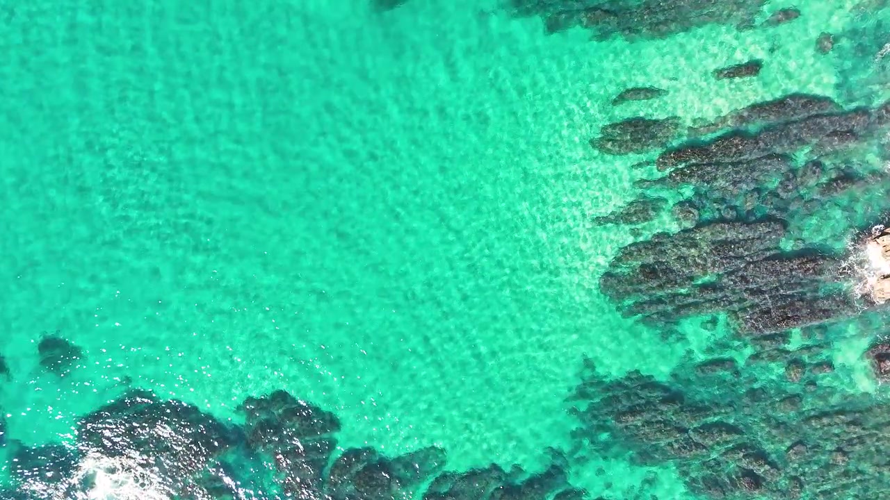 Vista aérea de cima para baixo de água turquesa límpida sobre rochas escuras submersas em Crescent Head, Austrália.
