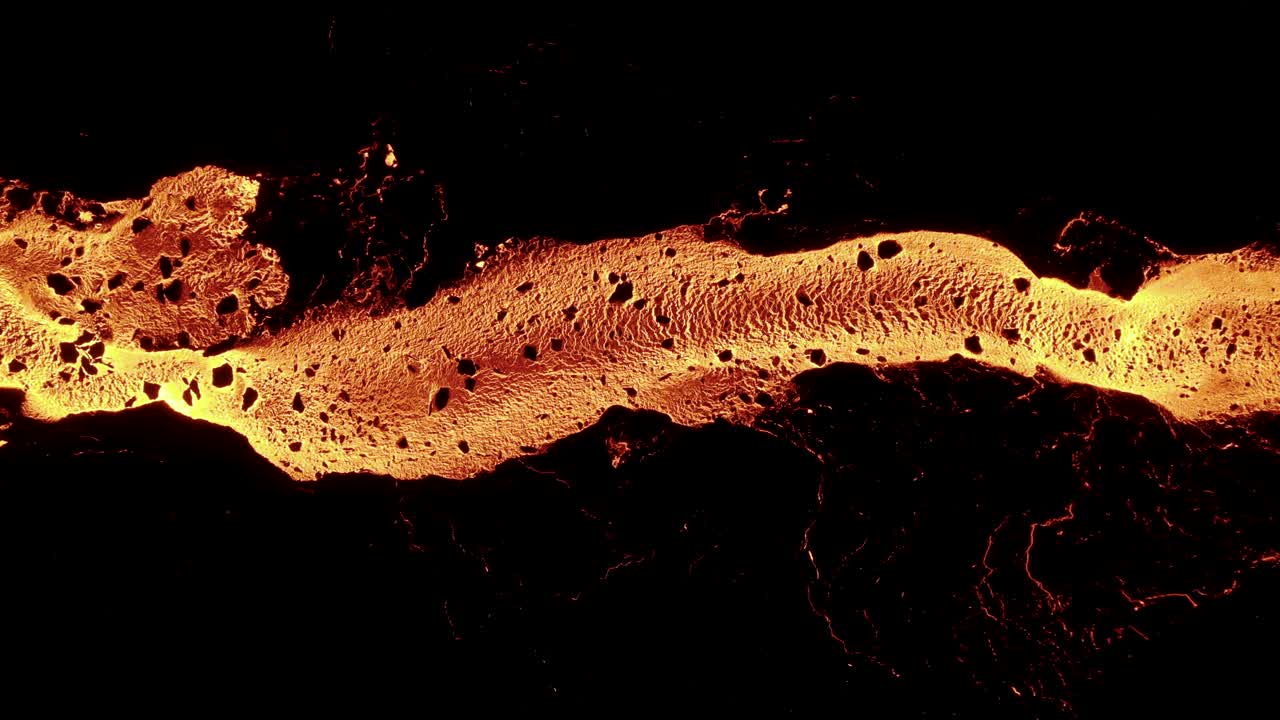 Fiume di lava fusa con un bagliore infuocato arancione di notte, roccia di basalto scura, vista dall'alto.