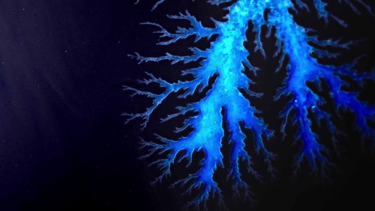 Bright blue ink forming intricate patterns and shapes resembling lightning branches on dark background