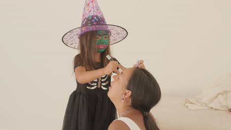 little girl in witch hat applying makeup on pregnant mother for halloween