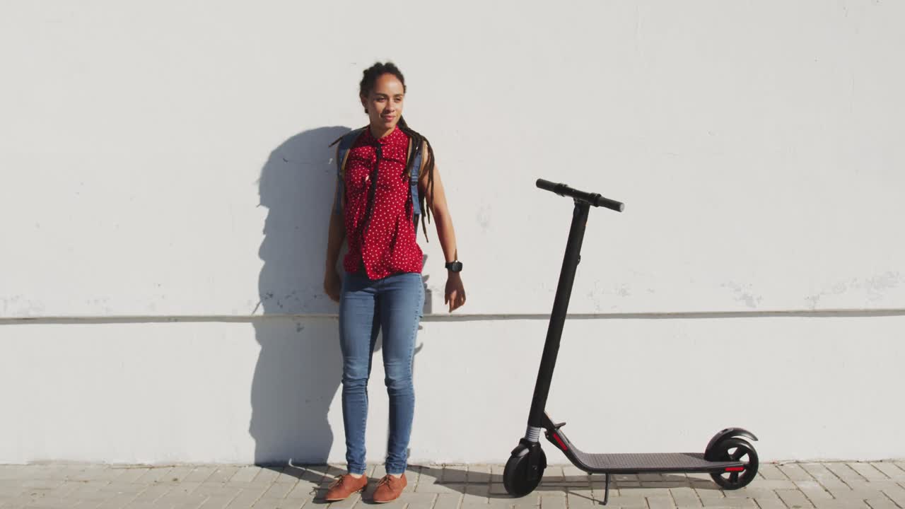 Mujer afroamericana de pie junto a un patinete en el paseo marítimo.