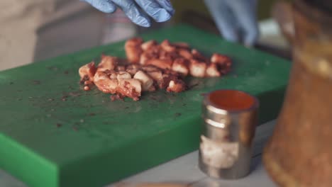 las manos del chef cortando pulpo cocido en una tabla verde