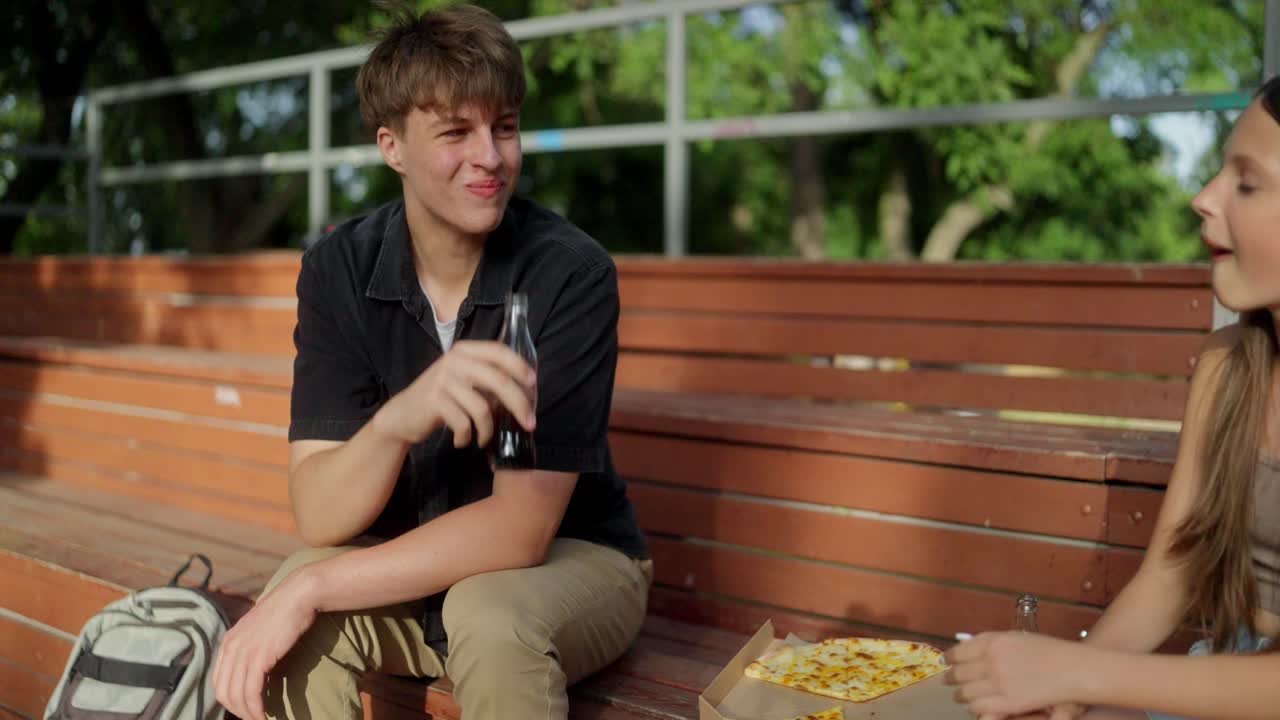 dos adolescentes disfrutan de una comida de pizza y refresco juntos en el parque