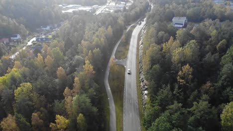 Drone-flying-over-road-through-Gothenburg-suburbs-with-woodland-areas
