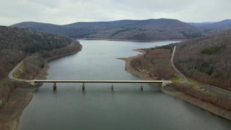 Drone-flying-toward-a-bridge-crossing-a-mountain-lake-in-a-valley-during-early-winter