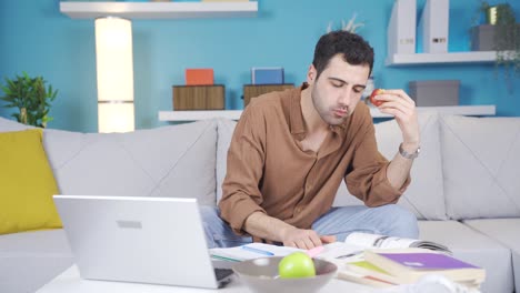 hombre joven trabajando en una computadora portátil en casa comiendo fruta.
