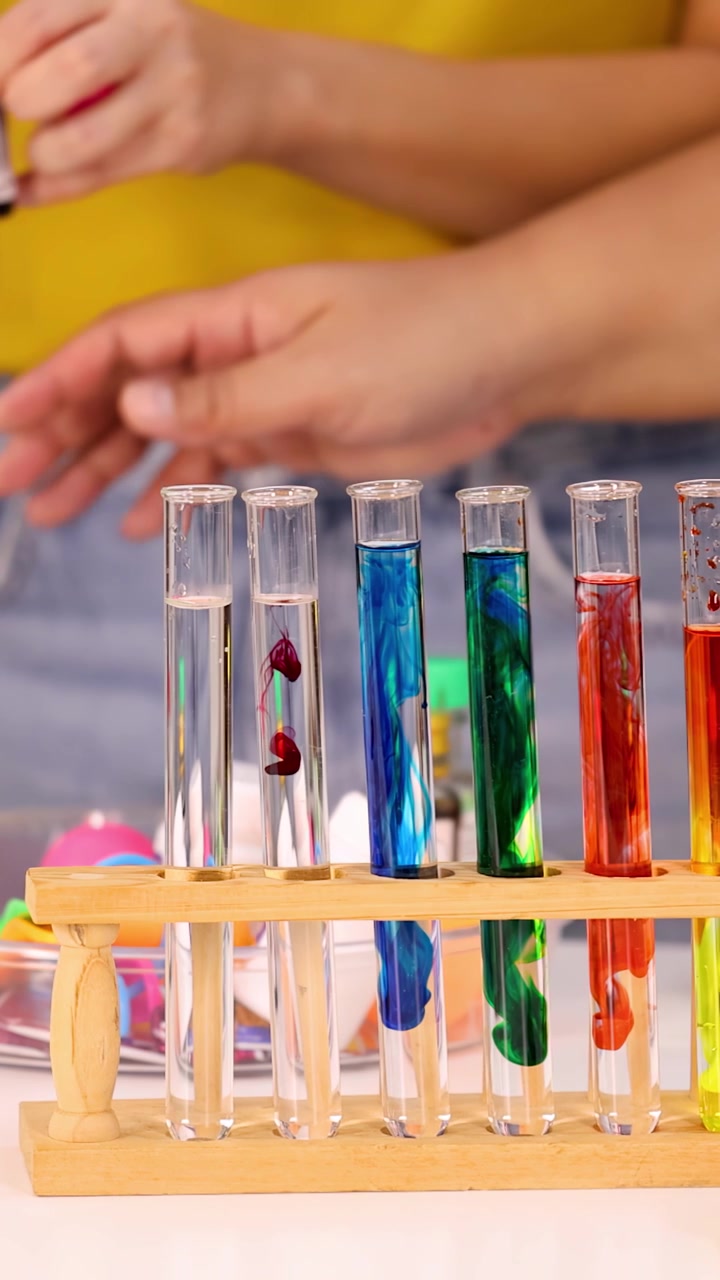 Close-up tangan menggunakan pipet untuk menambahkan cairan berwarna ke dalam tabung reaksi laboratorium