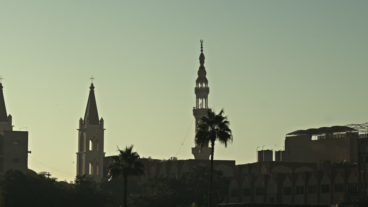 This sunset silhouette captures the St. Mary's Coptic Orthodox Cathedral and the neighboring minaret along the Nile riverfront in Luxor, Egypt
