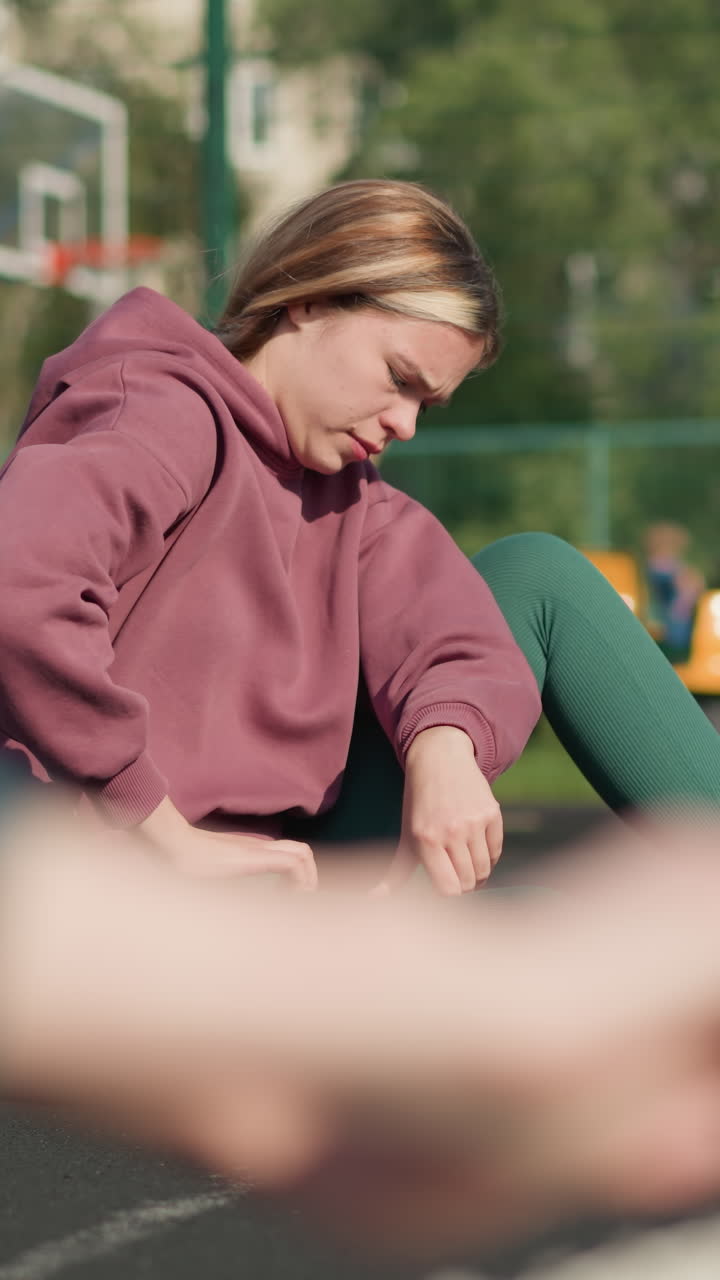 야외에서 운동하는 초록색 후디를 입은 여자의 클로즈업, 배경에 다른 두 여인이 스트레칭하고, 농구장과 스포츠 경기장에서의 피트니스 훈련을 특징으로합니다.