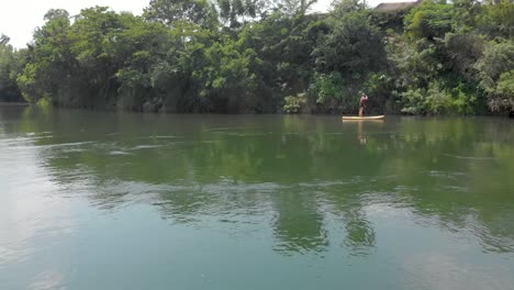 Aerial-shot-following-from-the-side-a-blonde-white-woman-on-a-stand-up-paddle-board-along-the-tropical-banks-of-the-river-Nile