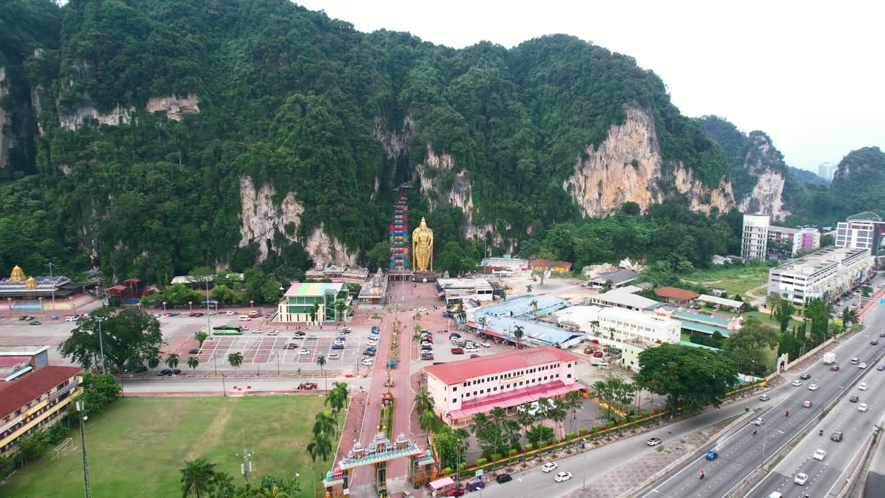 Pemandangan udara luas mengelilingi pintu masuk Gua Batu yang terkenal di Kuala Lumpur Malaysia pada sore yang mendung dengan lalu lintas jalan raya di dekatnya dan pegunungan kapur besar di kejauhan