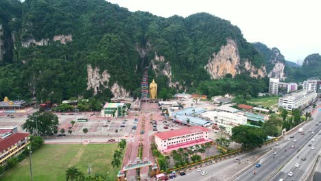 wide aerial circling the entrance to the famous batu caves in kuala lumpur malaysia on a cloudy afternoon with highway traffic nearby and large limestone mountains in the distance